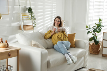 Happy woman with cup of drink relaxing on sofa at home