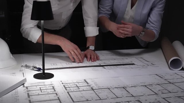 Architects collaborating on blueprints, diligently planning building design and construction project details late at night.