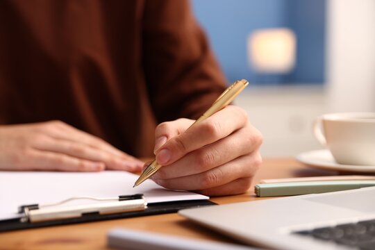 Woman writing in clipboard with pen at table, closeup