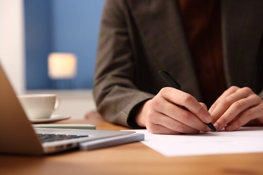Woman writing on sheet of paper with pen at table, closeup