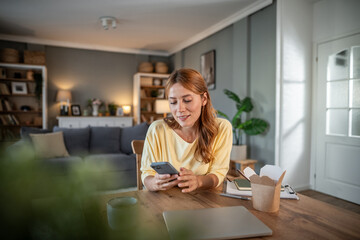 Woman using phone in home office with takeaway food