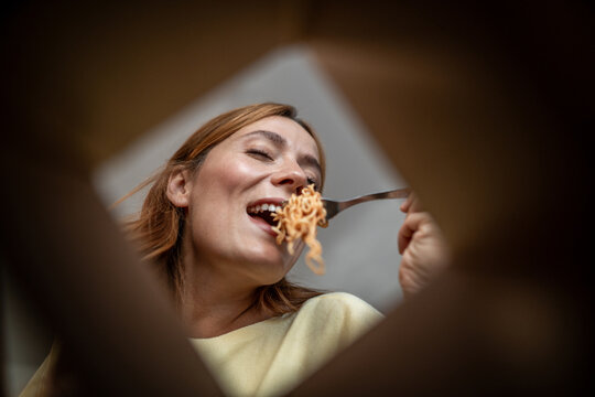 Happy woman enjoying take-out noodles from cardboard box