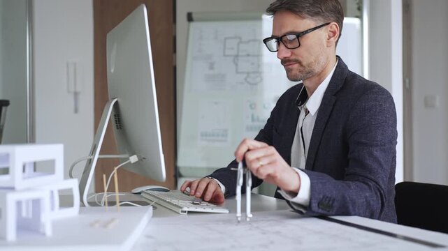 Male architect working on architectural blueprints, using a compass next to a computer while developing new building designs. Business and architecture concept