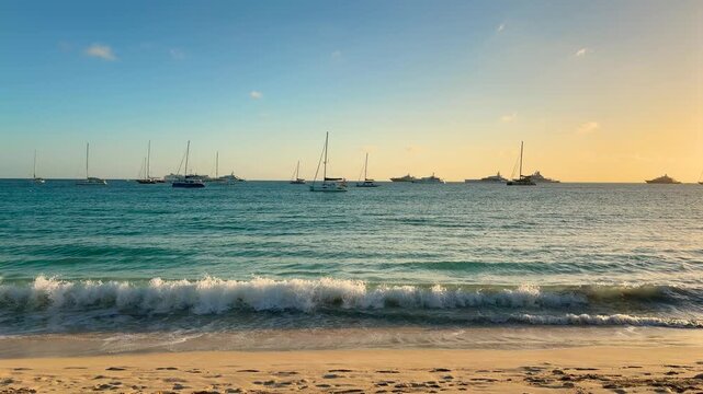 A view of the Caribbean Sea with moored sailboats in the distance from the island's sandy beach during a picturesque sunset. Island Saint Martin, the Caribbean.