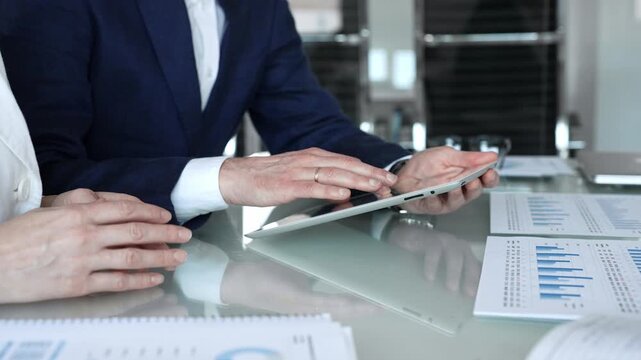Business partners collaborating on a digital tablet, analyzing financial data and reports during a corporate meeting in a modern office, planning strategies for growth
