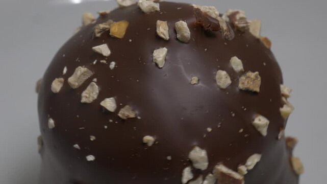 A close-up shot of a glazed dessert topped with crushed nut pieces, seen slowly rotating against a clean, neutral background.