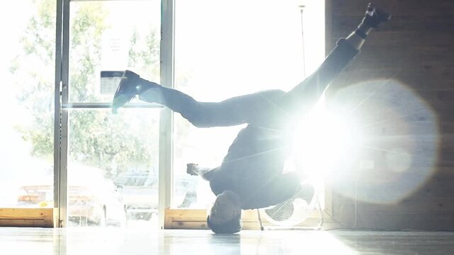 A slow-motion of a Caucasian guy breakdancing in a room