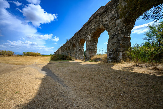 Preserved Roman aqueduct arches extend across terrain with pine trees in Parco degli Acquedotti, Rome.