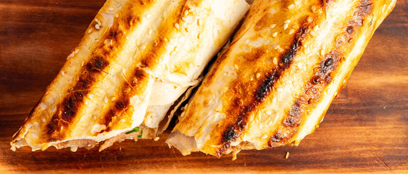 Delicious wraps with grilled bread and filling on a wooden board