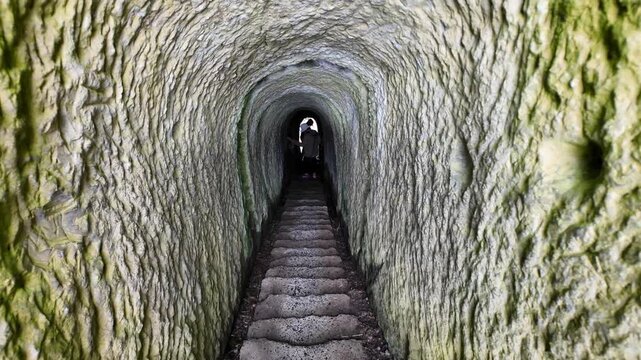 People walk through the famous hand-carved tunnel at Tunnel Beach, Dunedin, highlighting historic access, rugged coastal heritage, and the unique seaside experience in New Zealand.