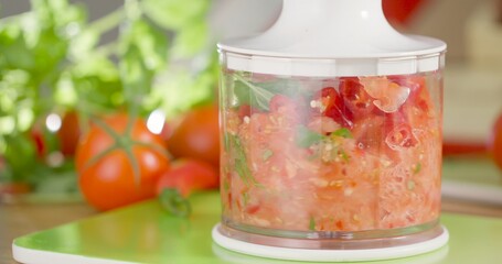 Chopping tomatoes and herbs in a food processor on a kitchen table with vegetables around © Joachim