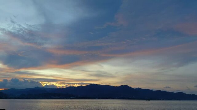 Golden sunset sky over dark mountain silhouettes and calm sea water with soft orange and blue gradients. Use for website header banners, YouTube cinematic intros, or travel vlogs.
