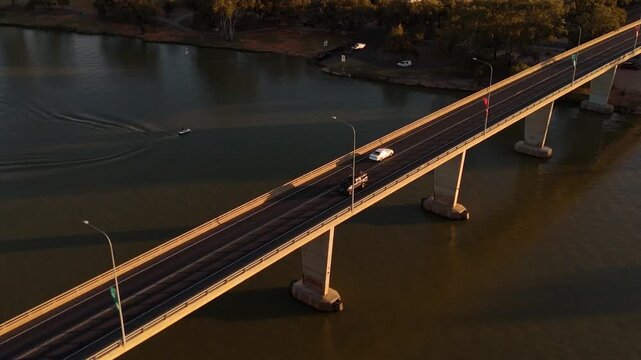 George Caffey Bridge spans the Murray River in Mildura with vehicles crossing calm water under warm golden light, aerial establishing orbit