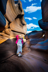 Woman in pink jacket explores narrow canyon with smooth rock walls and potholes under bright blue sky Lei Dan Stone Field Thailand