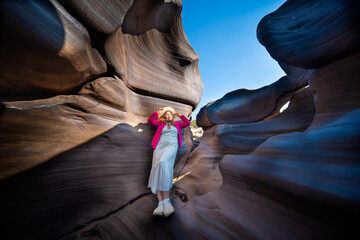 Young woman white dress and pink jacket exploring narrow canyon with smooth rock walls and potholes clear blue sky Lei Dan Stone Field Thailand