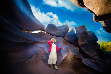 Woman standing in natural rock formation under bright blue sky with clouds and potholes creating unique shapes Lei Dan Stone Field Thailand