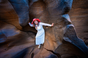 Woman in white dress and red hat explores smooth rock formations with potholes in narrow canyon with natural light Lei Dan Stone Field Thailand