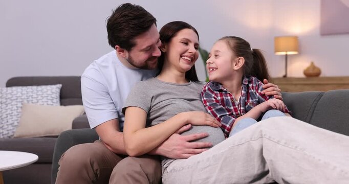 Pregnant woman, her husband and daughter on sofa at home