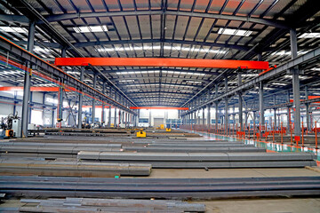 Obraz premium Spacious Steel Processing Factory Workshop with Overhead Cranes and Stacked Steel Profiles