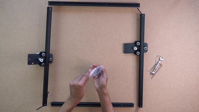Hands assembling laser engraver frame on tabletop, parts and tools neatly laid out