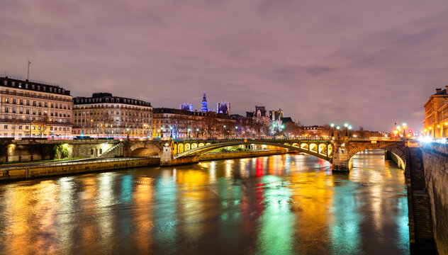 Pont Notre-Dame bridge crosses the Seine river with colorful city light reflections on the water during the evening in Paris, France