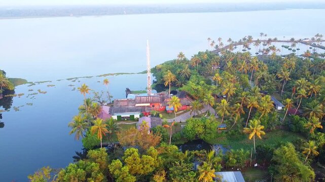Aerial drone shot of a scenic riverside house nestled among lush coconut groves and tropical greenery in the Kerala backwaters during a calm, golden sunrise.