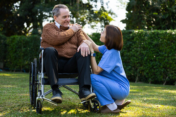 Friendly caregiver and senior man in a wheelchair sharing a joyful conversation outdoors, representing compassion and elderly support.