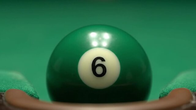Close-up view of a vibrant green number 6 billiard ball resting on a felt pool table.