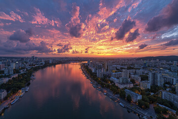 Fototapeta premium Sunset over city skyline with river reflecting vibrant orange and purple clouds, creating dramatic and peaceful urban atmosphere at dusk