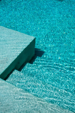 Vista detallada de una piscina con agua turquesa cristalina y reflejos de luz natural sobre superficie arquitect&oacute;nica moderna. Concepto de lujo, descanso, verano y estilo de vida relajado