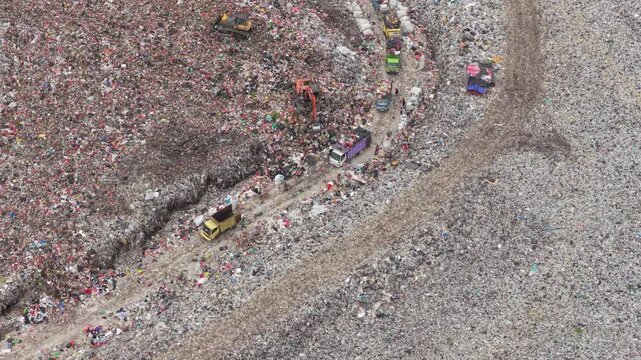 Top down aerial view of heavy machinery and queues of garbage trucks dumping plastic and household waste at a vast landfill, illustrating pollution, overconsumption and waste management crisis