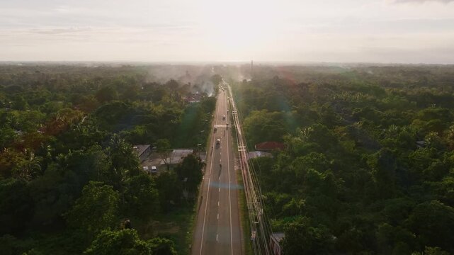 Straight roadway cuts through green landscape on Dauis Panglao National Road, symmetrical aerial dolly to sunset