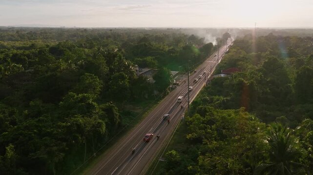 Traffic moving along Dauis Panglao National Road, aerial orbit at sunset in tropical forest