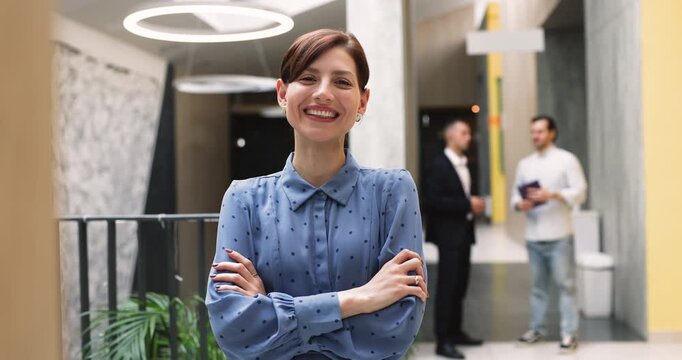 Business portrait of smiling young adult businesswoman, HR manager or team member standing with folded arms in corporate office, representing professional ambitions, achievements and career growth