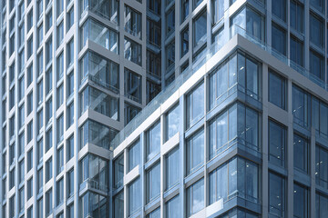 Fototapeta premium Modern glass curtain wall building exterior with reflective windows showing sky and clouds, creating sleek and professional urban architectural atmosphere