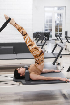 Woman training on pilates reformer with inversion technique, performing advanced flexibility exercise for core strength and spinal decompression therapy. Deep core activation and spine alignment