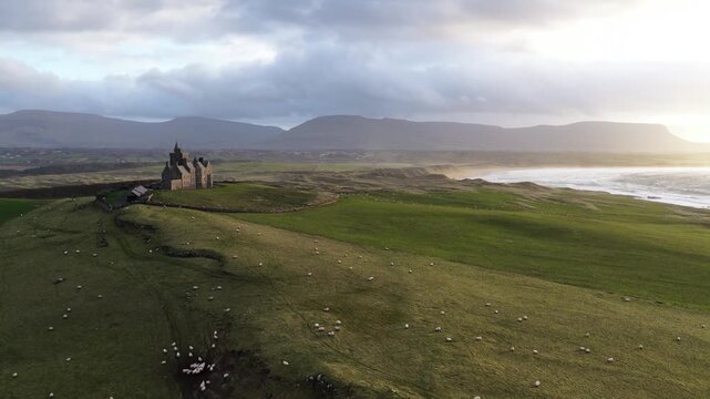 Cinematic drone footage of Classiebawn Castle at Mullaghmore Head, Ireland, glowing at sunset as sheep graze across green fields along the dramatic Atlantic coastline.