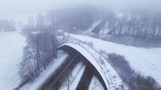 Aerial ascending movement showing contrasting Dutch snow landscape with environment nature reserve infrastructure ecoduct in hazy winter conditions