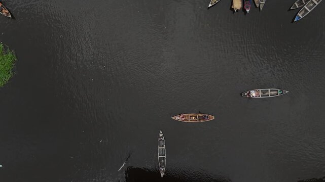 A cinematic top-down aerial shot capturing traditional wooden boats navigating the dark waters of Lake Nokoue in Ganvie, Benin