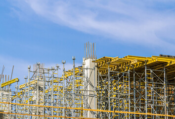 concrete building under construction. scaffolding and steel framework on blue sky background.