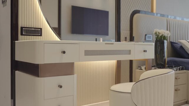 Modern elegant vanity table with drawers, curved mirror, upholstered chair, and soft lighting. Tilt up shot.