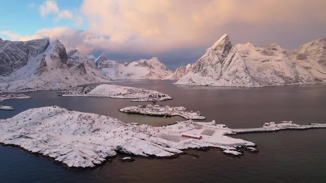 Cinematic 4K drone shot of Sakrisoy with norwegian traditional cabins and Anita Sjomat. E10 road against snow capped Reinefjorden mountains at Arctic sunset.