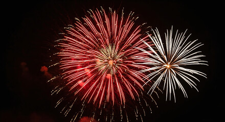 Vibrant fireworks exploding in the night sky with red and white sparks.