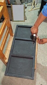 Person using a manual staple gun on a black wooden structure.