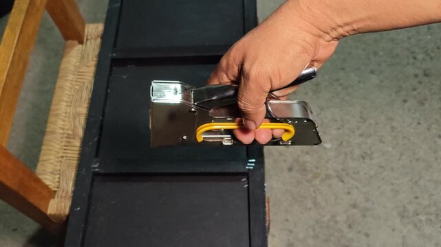 Yellow manual staple gun being used on a black wooden frame.