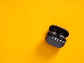 Wireless earbuds in charging case on yellow background