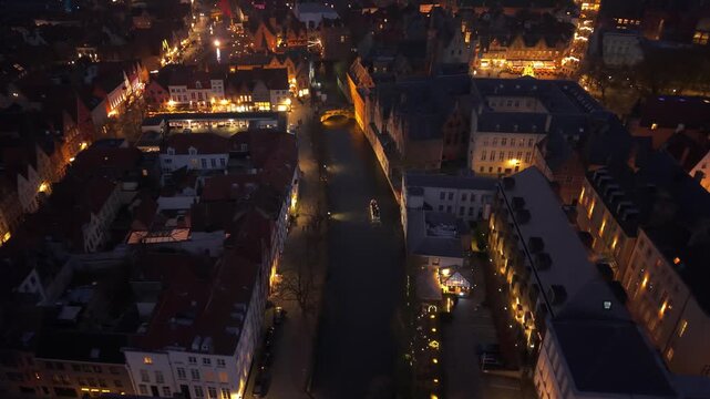 Night view of Bruges decorated for Christmas, with illuminated canals and a tourist boat passing through the festive city center.