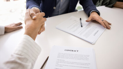 Close up image of two men firmly shaking hands over desk, symbolizing successful closing of business deal, seated at table with signed contract papers. Trust, commitment and professional partnership © fizkes