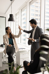 Young professional male, female team members giving each other high five after successful teamwork,...
