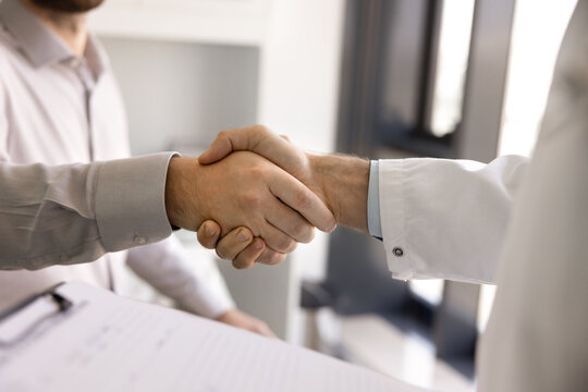Trust and collaboration in healthcare. Close up male doctor wear white coat shake hands with patient pharma representative administrator. Professionalism cooperation in medical care service concept